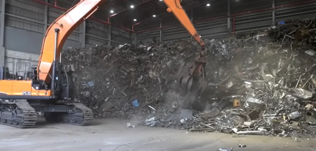 Material handler grapple loading demolition scrap inside a recycling warehouse